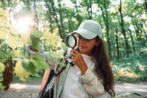 Using magnifying glass. .Girl ,is in the forest at summer day time discovering new places photo