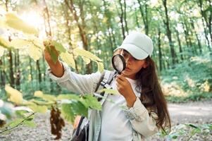 Using magnifying glass. .Girl is in the forest at summer day time discovering new places photo