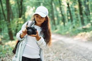 Standing and holding ,camera in hands. Girl is in the forest at summer day time discovering new places photo