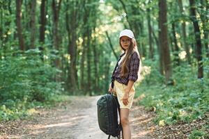 Holding the backpack. Girl is in the forest at summer day time discovering new places photo
