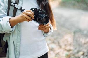 Standing and holding camera in hands.. Girl is in the forest at summer day time discovering new places photo