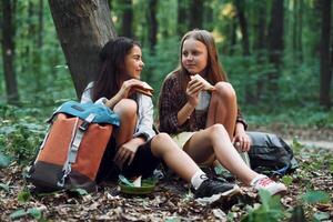 Eating .by using plastic forks and plates. Two girls is in the forest having a leisure activity, discovering new places photo