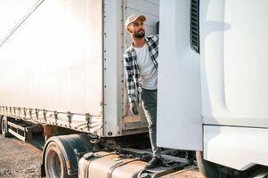 Standing behind the cabin. Young ,truck driver is with his vehicle at daytime photo