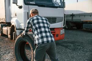 Working with wheels. Young truck driver is with his vehicle at daytime, photo