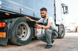Holding notepad. Quality, control. Man in unifrom doing service for big truck vehicle photo