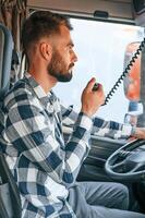 Using radio. .Young truck driver is with his vehicle at daytime photo