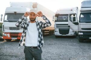 Front view. In cap. Young truck driver ,is with his vehicle at daytime photo