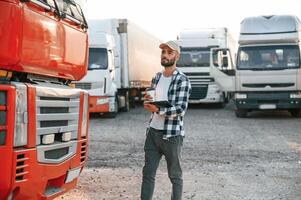 With cup .of drink and notepad. Young truck driver is with his vehicle at daytime photo