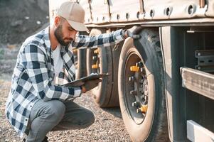 Working with wheels. Young truck driver is with his vehicle at daytime photo