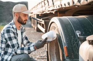Testing the tires. Young truck driver is with his vehicle at daytime photo