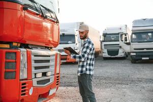 Looking at document in notepad. Young truck driver is with his vehicle at daytime photo