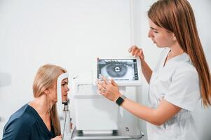 Side view. Woman's vision is tested by clinic worker that using special device. photo