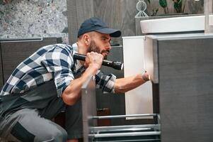 Using, flashlight. Plumber in uniform is indoors at home photo