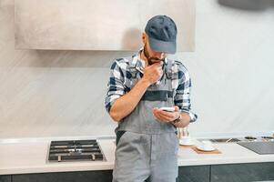 Holding ,smartphone in hand. Plumber in uniform is indoors at home photo