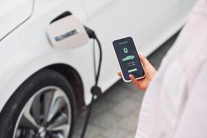 Close, up view. Woman charging her electric car and monitoring process on smartphone photo