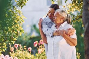 Embracing and smiling. .Young woman is with her senior mother is in the garden photo