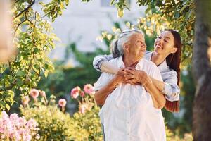Standing in the beautiful garden and embracing each other. Young woman is with her senior mother photo