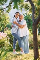 Embracing and posing, for a camera. Young woman is with her senior mother is in the garden photo