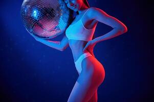 With shiny, mirrored ball. Young woman in underwear is in the studio with neon lights photo