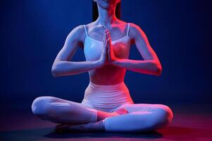 Lotus pose. Young, woman ,in sportive clothes is in the studio with neon lights photo
