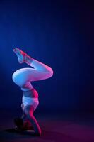 Doing head stand. .Young woman in sportive clothes is in the studio with neon lights photo