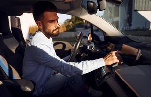 Man is sitting in the vehicle. Young stylish guy is with electric car at daytime photo