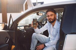 Monitoring ,charging procces by ,using smartphone. Young stylish man is with electric car at daytime photo