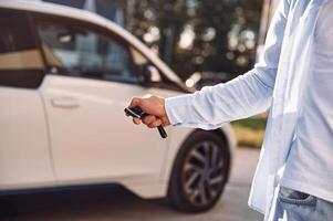Standing with keys and locking the automobile. Close up view of man with his electric car photo
