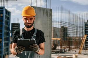 In hard hat, with notepad. Man in uniform is working on the construction site photo