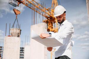 With ,plan in hands. Man in uniform is working on the ,construction site photo