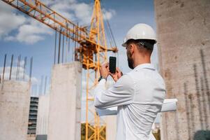 Taking a picture of place by smartphone. Man in uniform is working on the construction site photo
