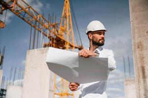 With plan in hands. Man in uniform is working on the construction site photo