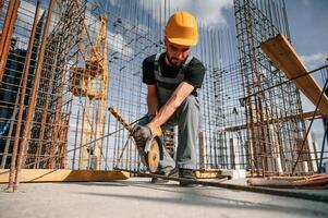 Using grinding, machine to cut metal pieces. Man in uniform is working on the construction site photo