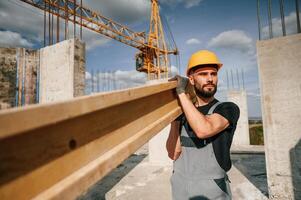 Front view of man, that is in uniform holding wooden plank on the construction site photo