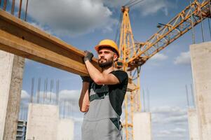 Front view of man that is in uniform holding wooden plank on the construction site photo