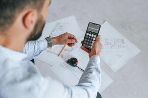Calculating numbers by using smartphone. Plan is on the floor. The man is making repairs in the apartment photo