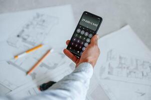 Calculating ,numbers by using smartphone. Plan is on the floor. The man is making repairs in the apartment photo