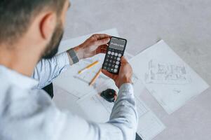 Calculating, numbers by using smartphone.. Plan is on the floor. The man is making repairs in the apartment photo