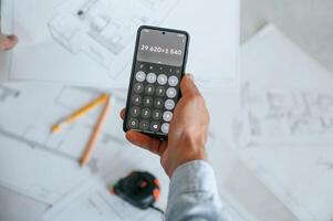Calculating numbers by using smartphone. .Plan is on the floor. The man is making repairs in the apartment photo