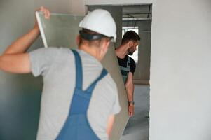 Moving construction pieces by hands. Two men is making repairs in the apartment together photo