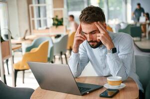 Feeling ,bad and tired. Young man ,is sitting in the cafe and working by using laptop photo