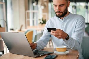 Making, payment by credit card. Young man is sitting in the cafe and working by using laptop photo