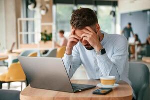 Feeling bad and tired. .Young man ,is sitting in the cafe and working by using laptop photo