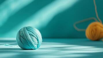 pale blue wool yarn ball is centered on turquoise surface with soft shadows photo