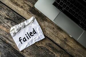 Crumpled paper with failed written on it beside a laptop reflecting fear and aspiration in a workspace photo