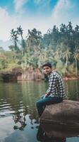 Man sitting on rock in water with trees in background photo
