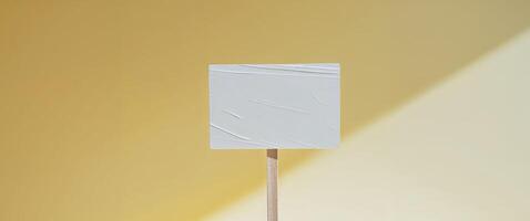 A white square on a stick in front of a yellow wall photo