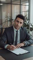 A man in a suit sitting at a desk with a pen and paper photo