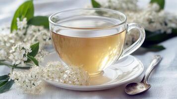 Transparent cup of herbal tea with blossoms on white cloth and silver spoon photo