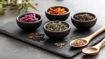 Assorted loose leaf teas and herbs in bowls on slate tray with wooden spoons photo